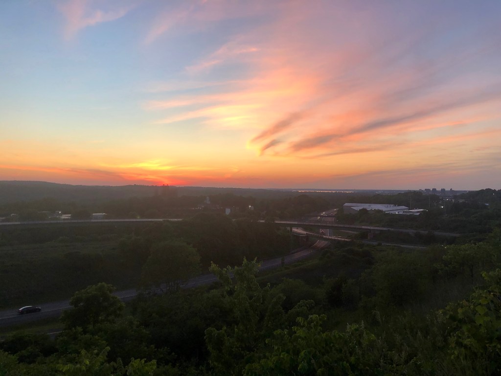 Super colorful sunset with pastel and wispy clouds over Syracuse, New York, with the J.M.A. Wireless Dome and Route 81 in the background.