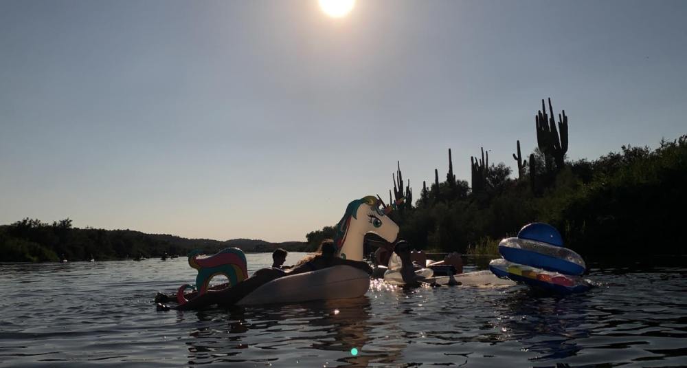 a dark silhouette photo of a a group of friends floating down the Salt River in Arizona, saguaro cacti line the horizon