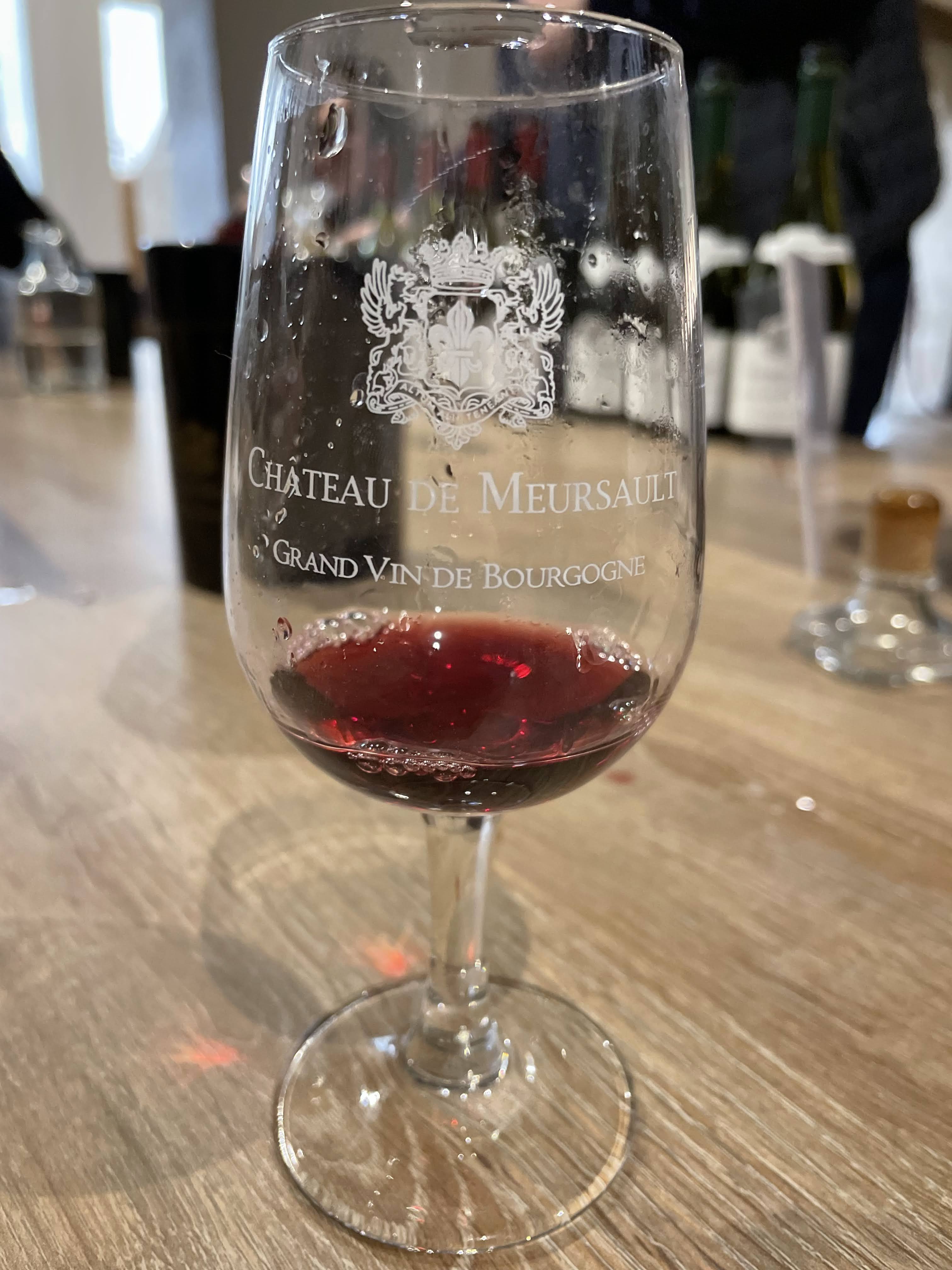 A wine glass with an engraving saying "Chateau de Meursault" holding red wine