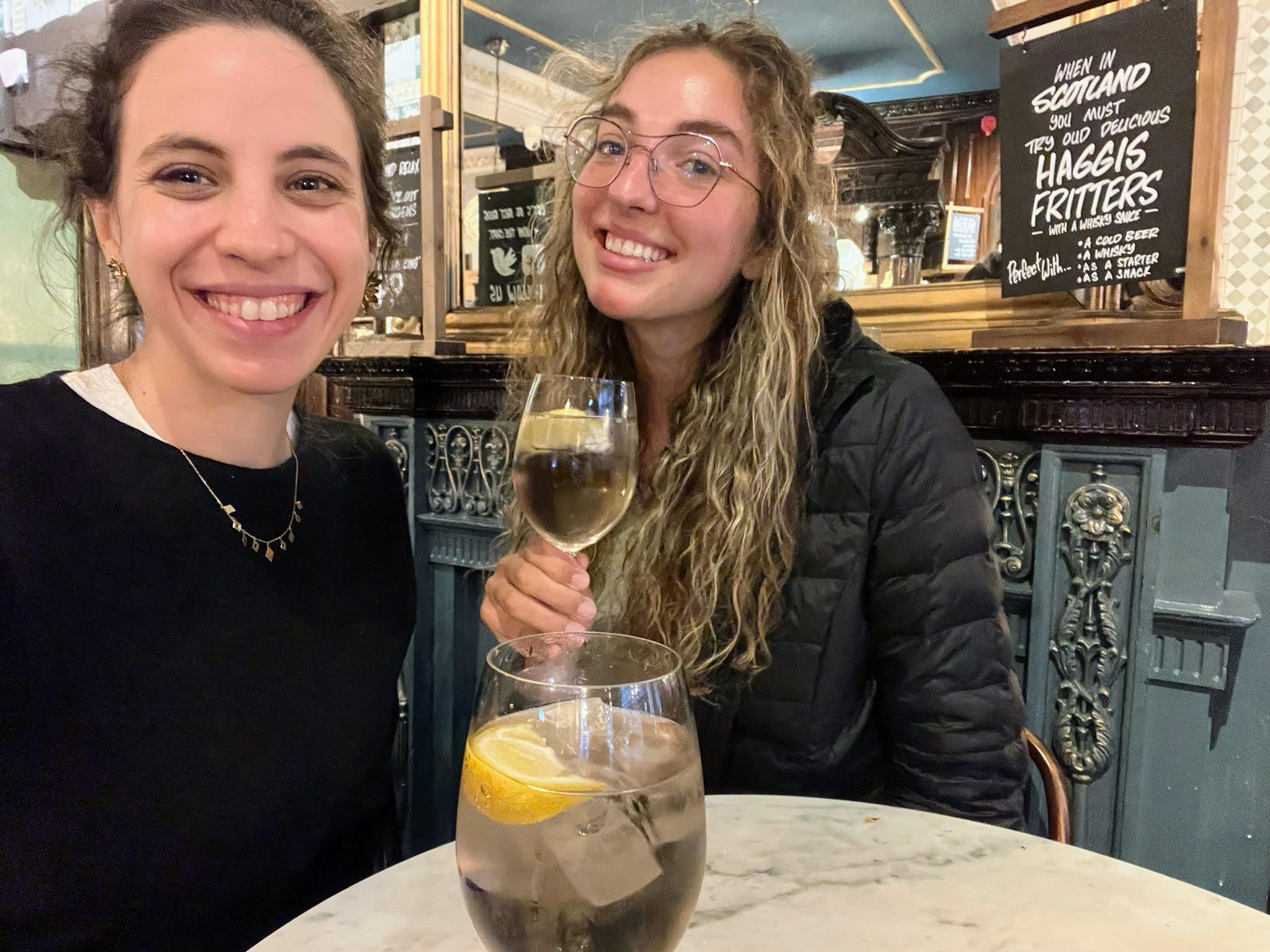 two girls smiling and holding a gin and tonic in a pub in Scotland