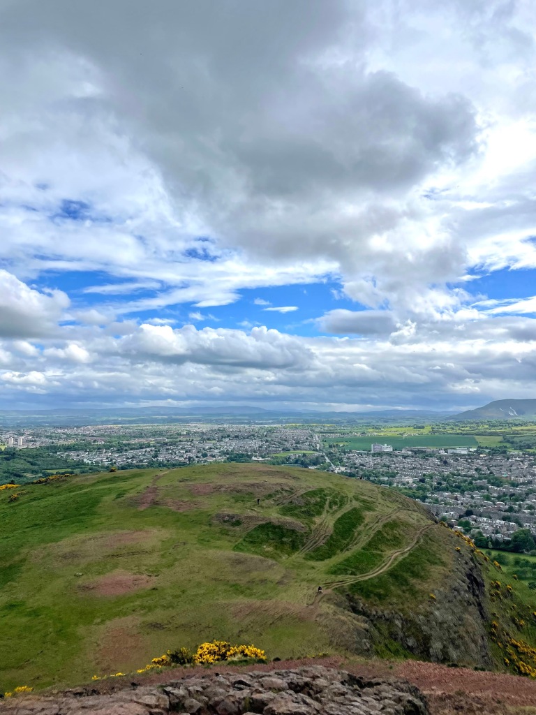 view of the north sea from the top of arthur's seat in Edinburgh, Scotland. green rolling hills, blue skies, houses below
