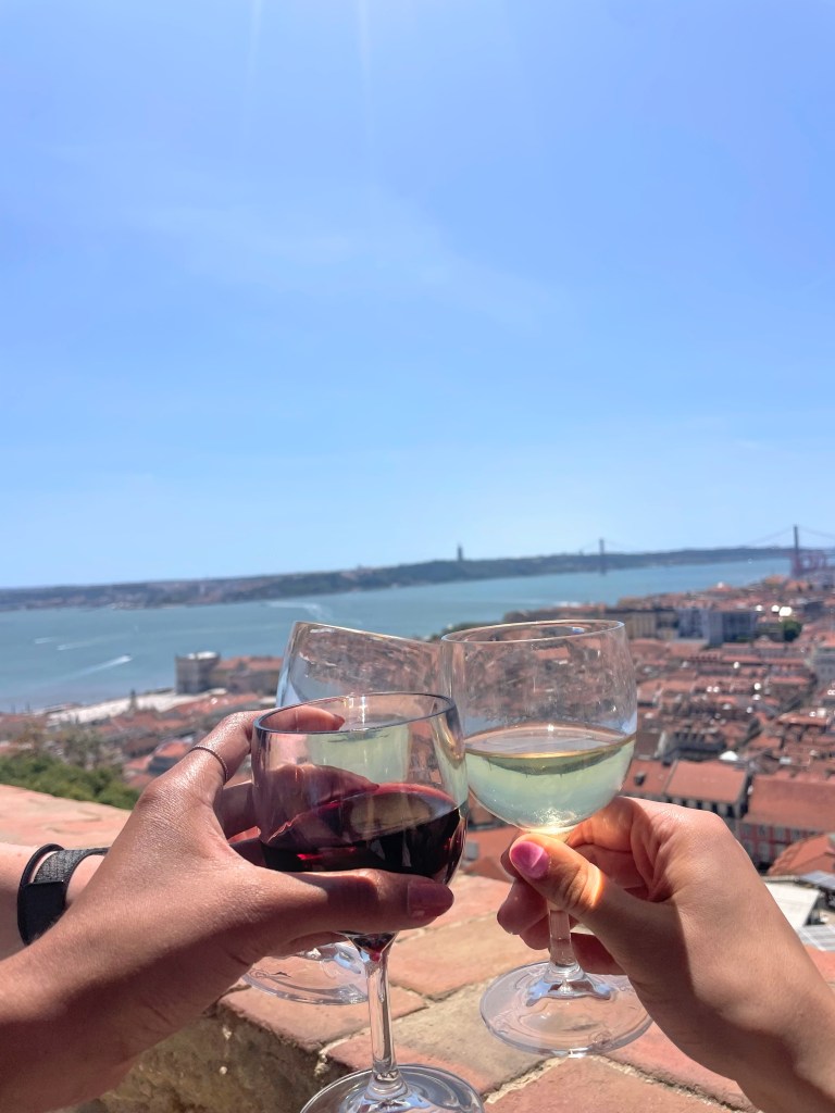 three wine glasses clinking with a view of the Tagus River in Lisbon, Portugal