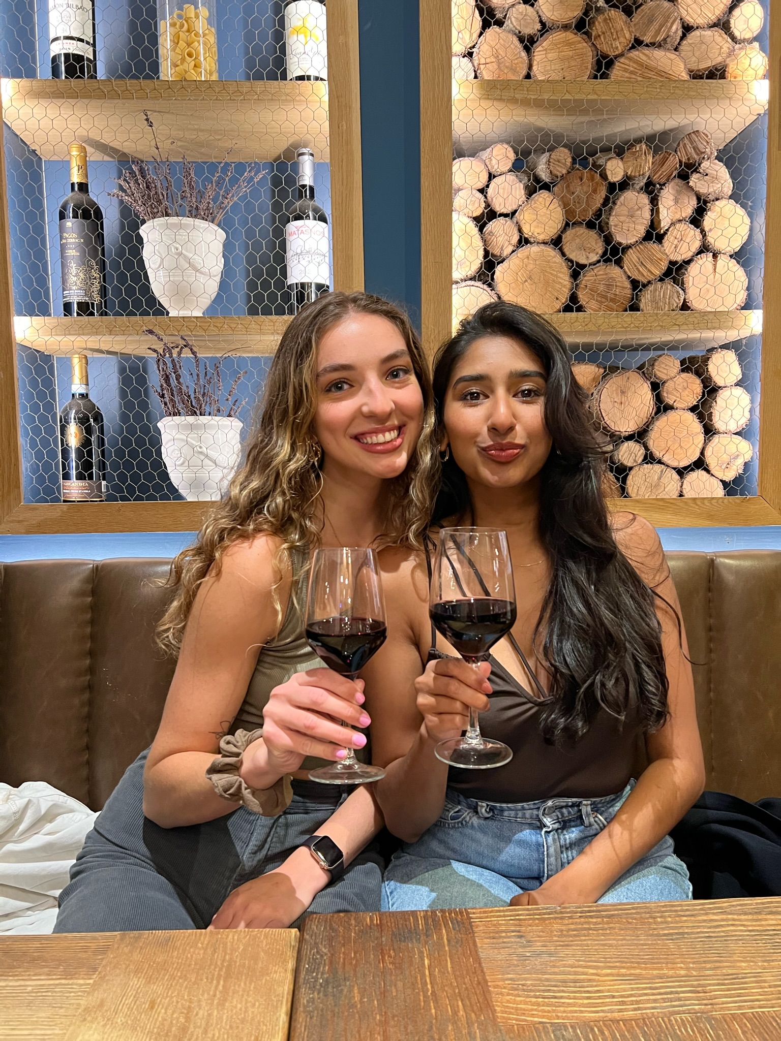 Two girls smiling while holding a glass of red wine in an Italian restaurant in Madrid, Spain