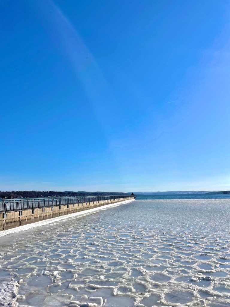 Skaneateles Lake frozen over during the winter on a clear, blue sky day.