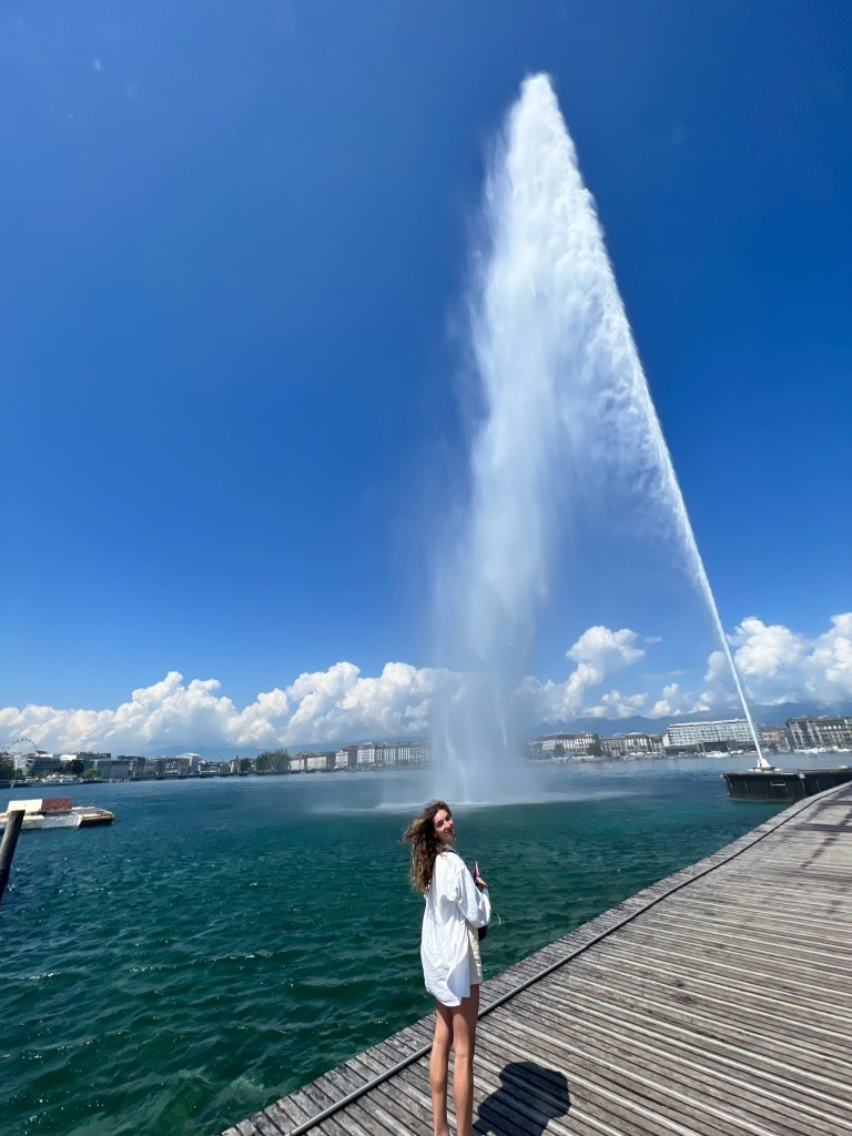 A tall girl standing next to the jet d'eau at Lac Geneva in Switzerland