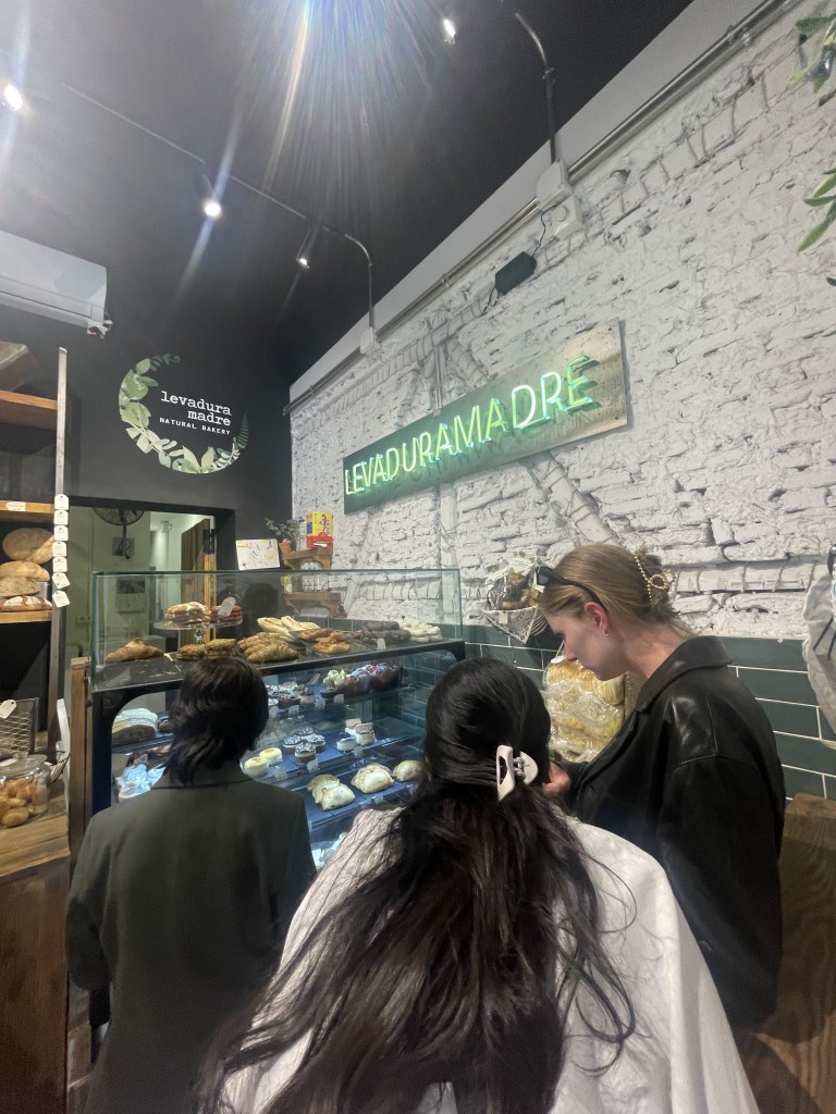 Photo of three girls deciding what to order, in front of a bakery display case in Madrid, Spain