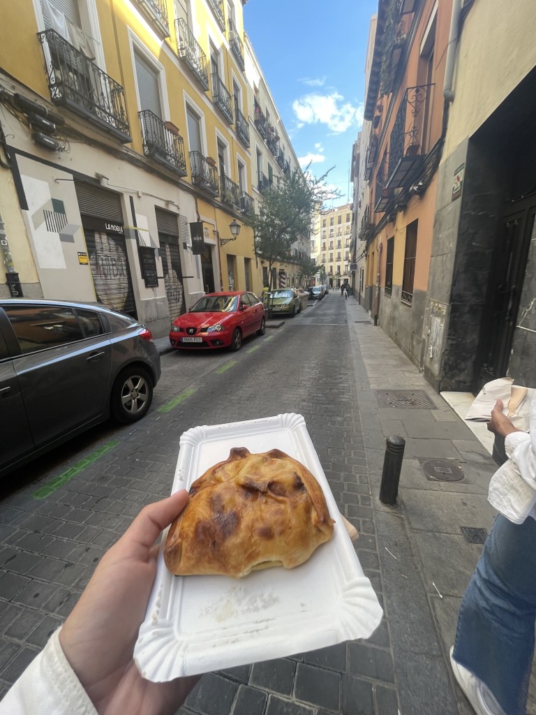 Photo of a woman's hand holding an empanada as she walks through the streets of Madrid, Spain