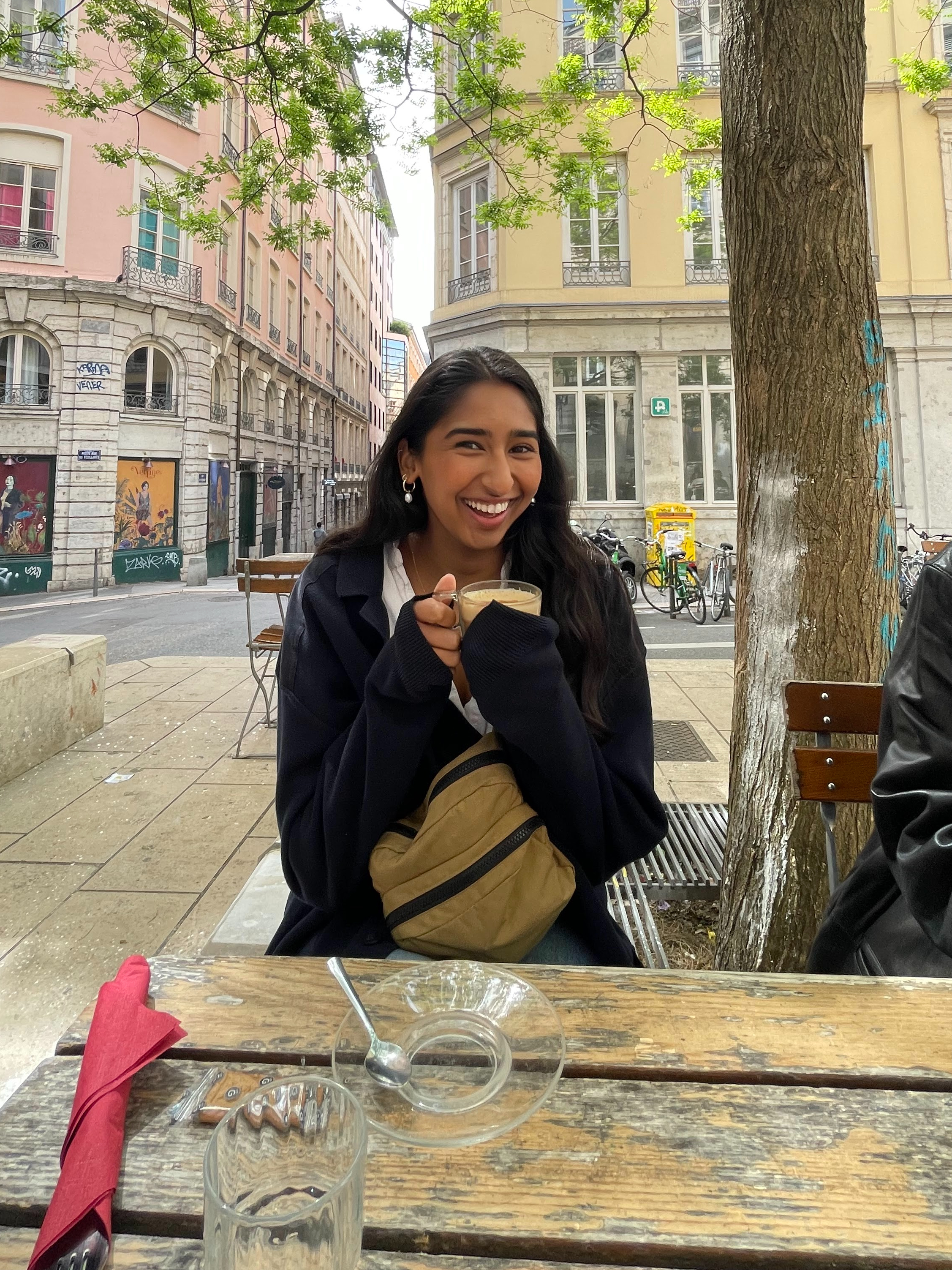 a girl laughing and hugging her hot chai latte while sitting at an outdoor café in Lyon, France