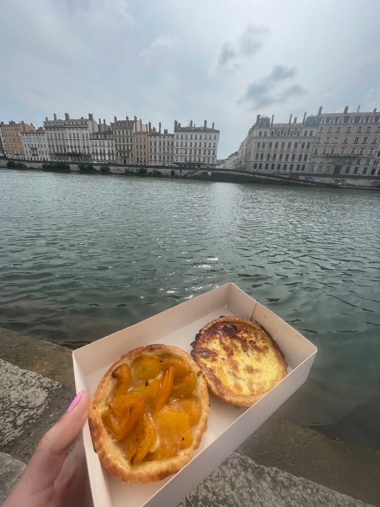A small box containing a tarte with apricots and a quiche lorraine, with the Saône river in the background