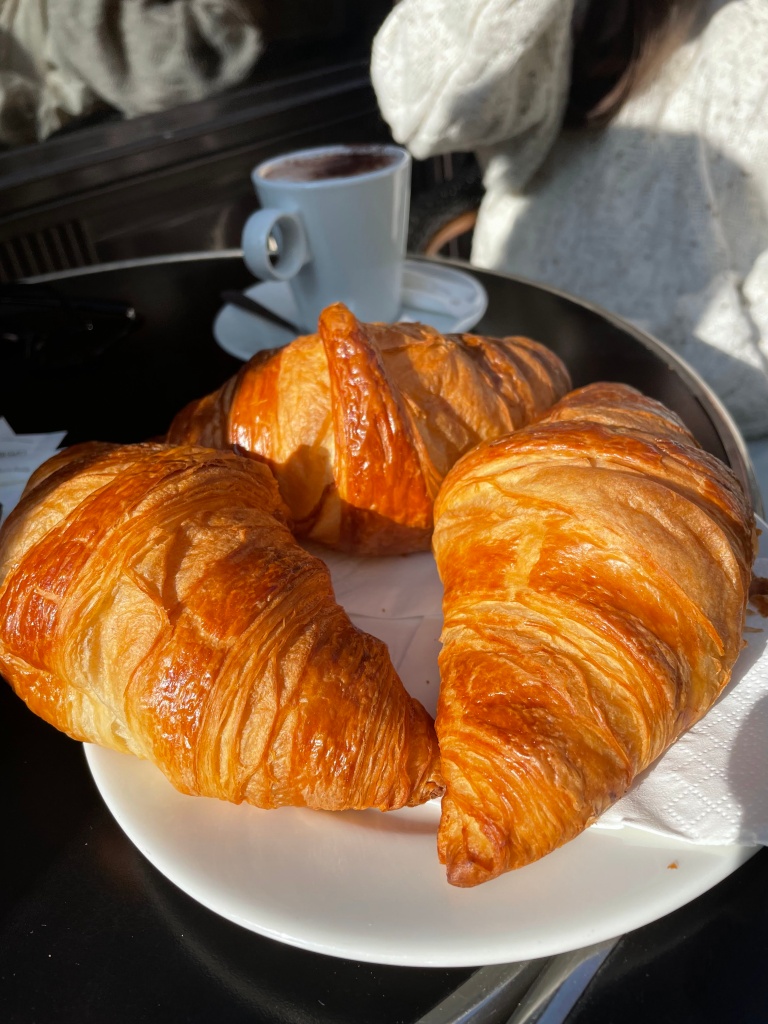 A plate of three golden buttery croissants in great lighting from the sun, outside at a cafe in Paris