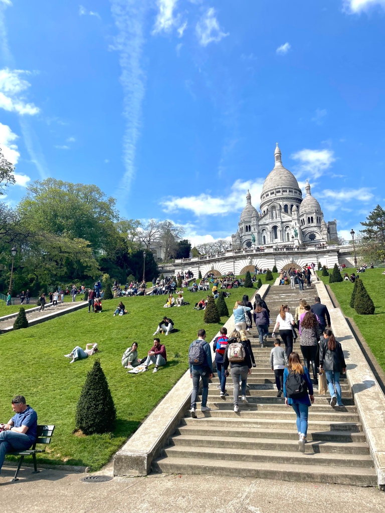 The steps leading up to Sacré Cœur basilica on a very clear, blue day, with people hanging out in the grass and relaxing.