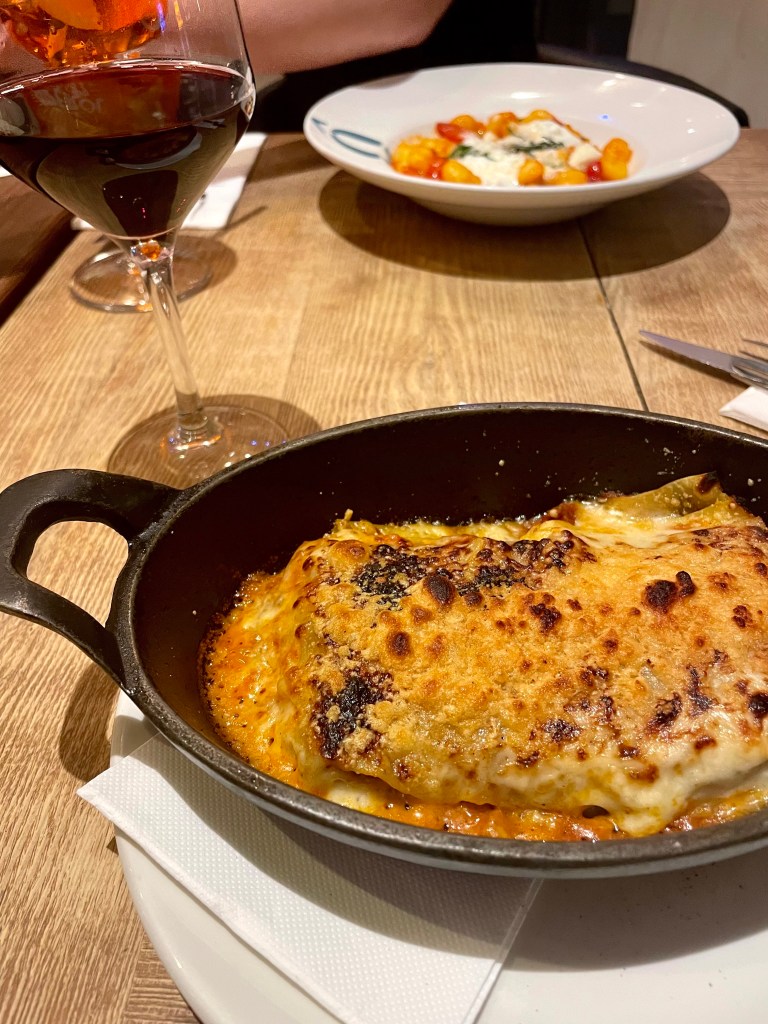 Lasagna bolognese served in a skillet, plated next to a glass of red wine at an Italian restaurant in Madrid