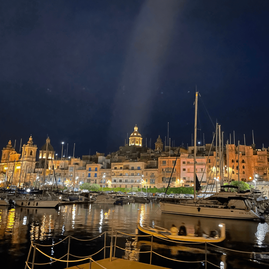The buildings of Malta lit up during the night, reflecting off of the marina on a beautiful, clear sky night.