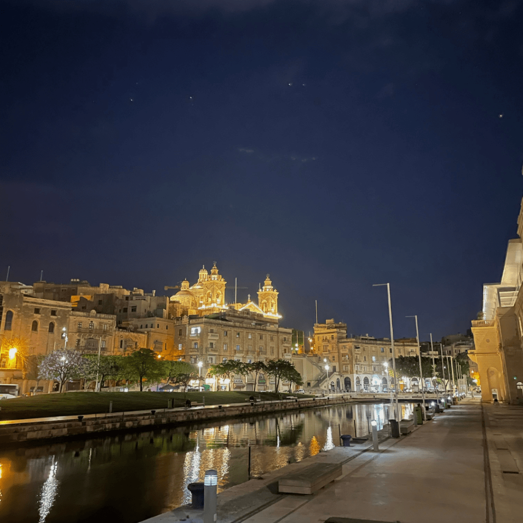 A beautiful church on the island of Malta lit up during the night, reflecting off of the marina on a beautiful, clear sky night.