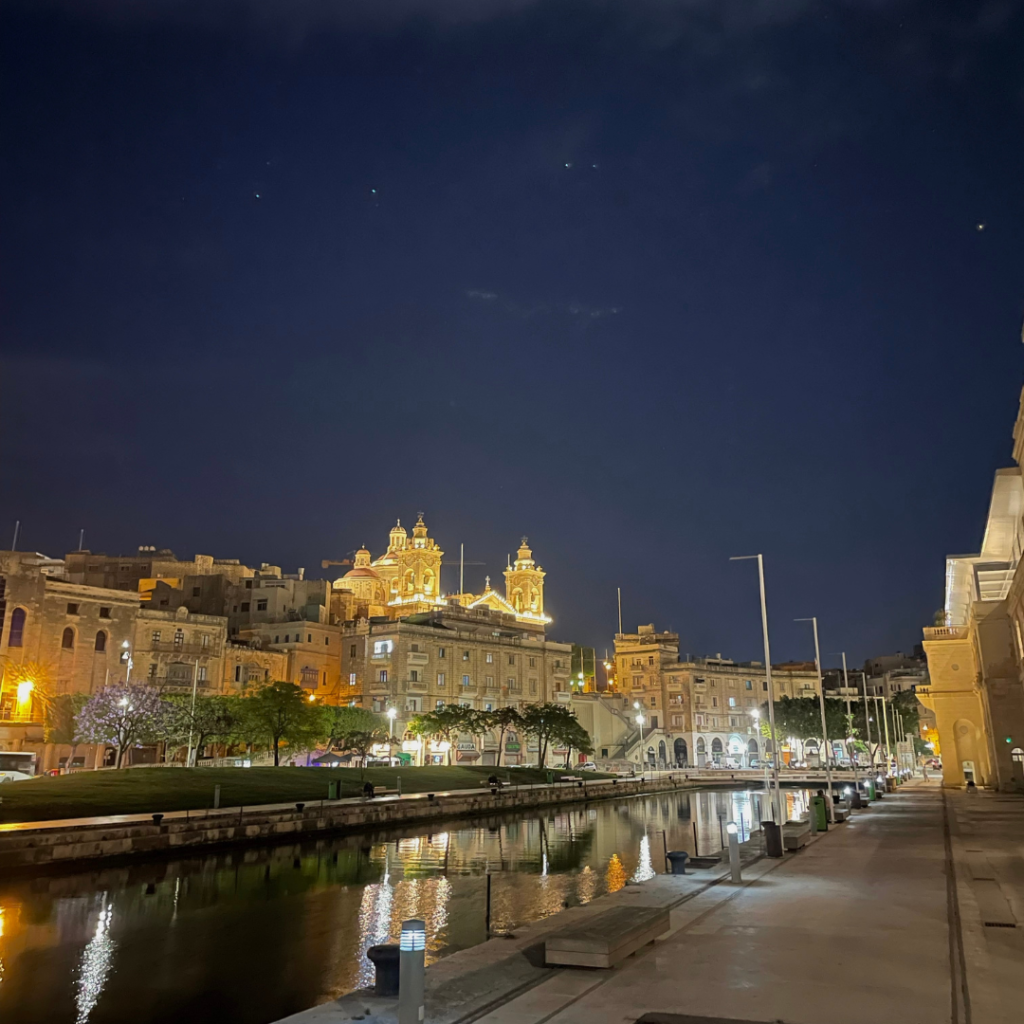 A beautiful church on the island of Malta lit up during the night, reflecting off of the marina on a beautiful, clear sky night.