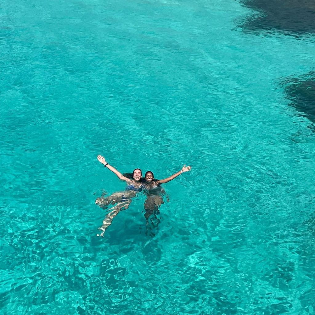 Two best friends swimming in crystal clear waters at the Blue Lagoon while budget backpacking on the island of Malta in Europe
