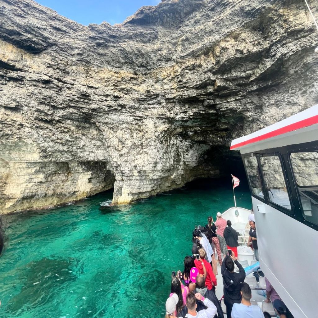 A small day cruise ship heading towards a cave in clear, turquoise waters while on a day cruise off of the island of Malta