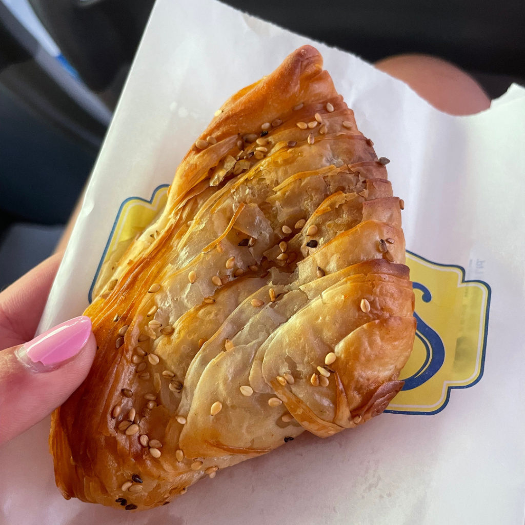 A woman's hand holding the most famous Maltese street food, a pastizzi, topped with sesame seeds