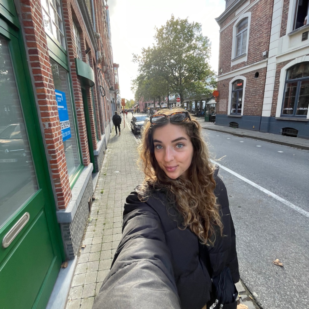 A girl taking a .5 selfie with a new black puffer jacket while walking the streets of Bruges, Belgium