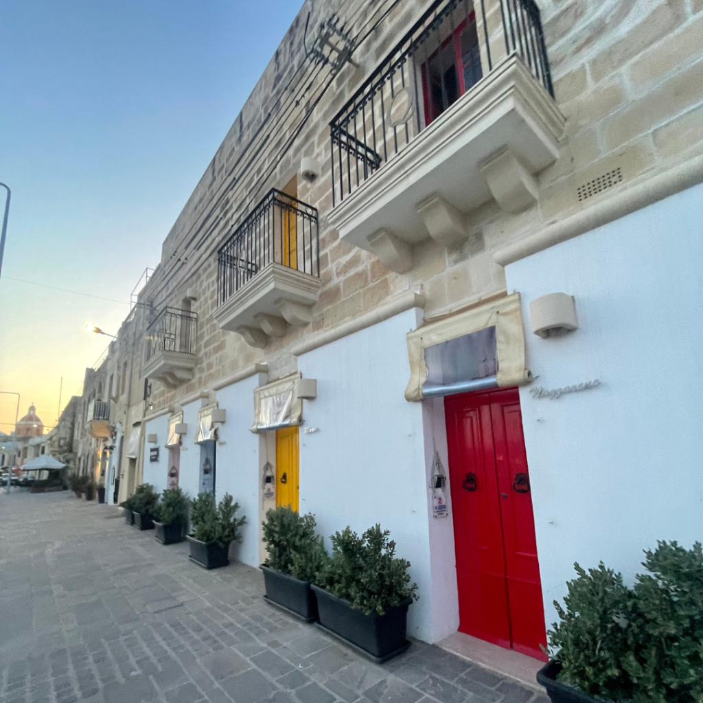 Pastel yellow sunset setting over the limestone buildings with cute, colorful doors on the island of Malta