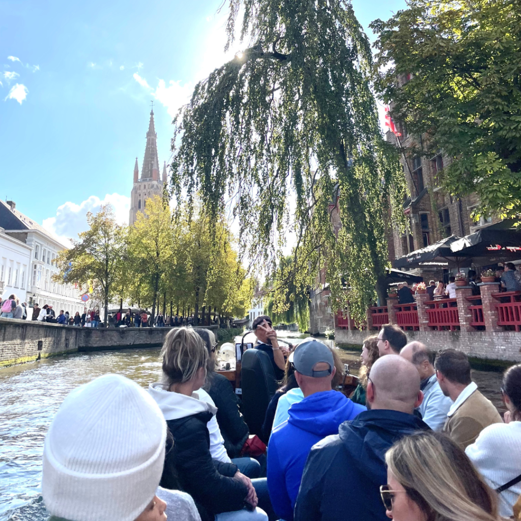 A tour group on a boat exploring the canals in Bruges, Belgium with a tower in the background on a sunny day