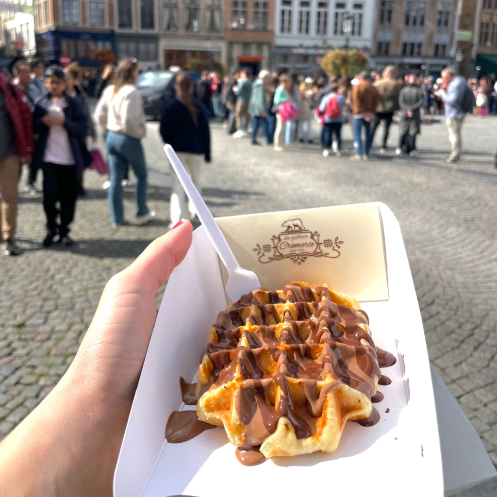 A hand holding a liege waffle topped with Belgian chocolate at Grotes Markt in Bruges, Belgium