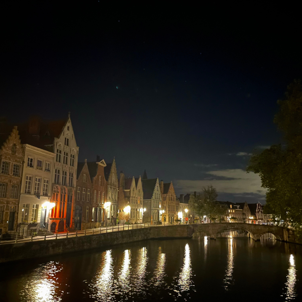 The canal at night in Bruges, Belgium, with the buildings lining the canals and lit up by front door lights