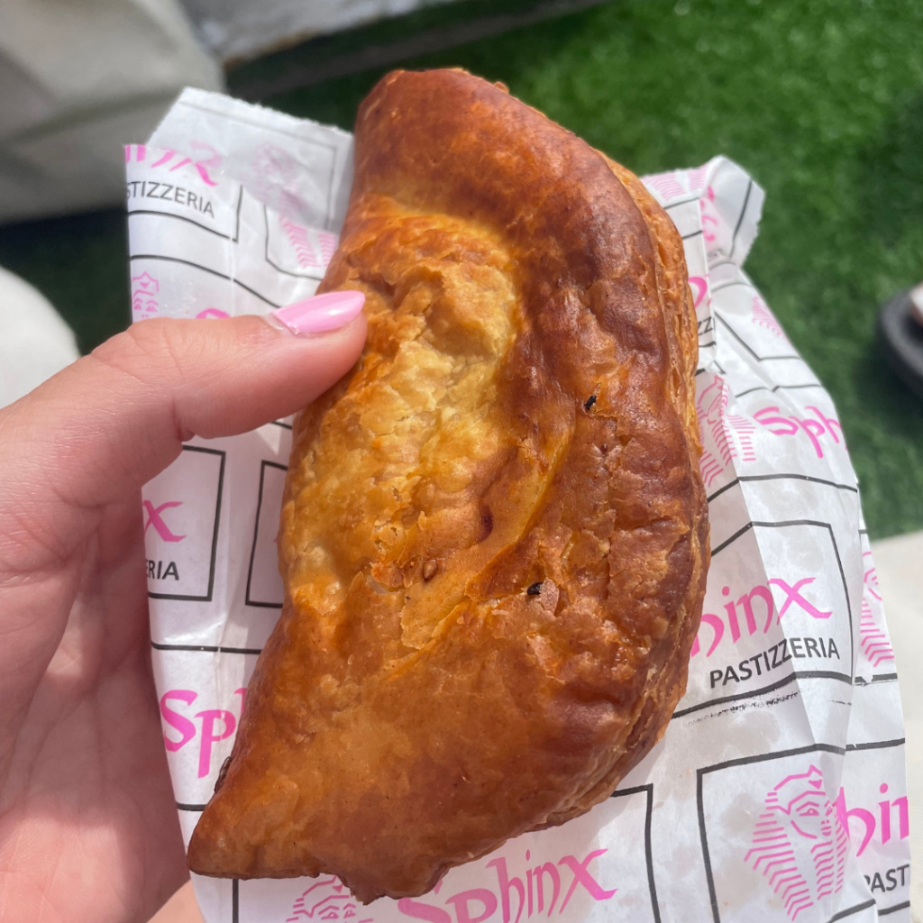 A hand holding a fried breakfast pastry filled with refried beans from a Pastizzeria on the island of Malta