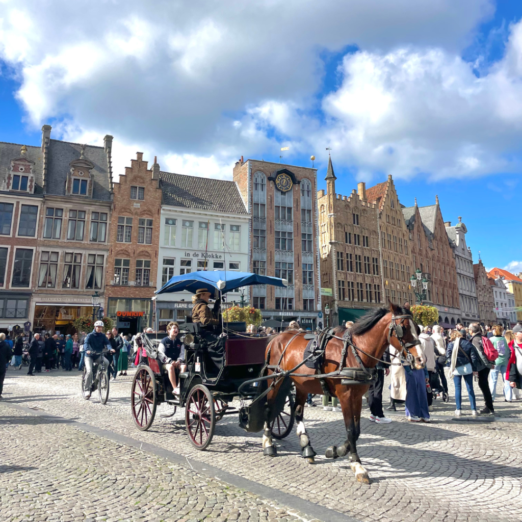A horse and carriage making it's way through the Market Square in Bruges, Belgium on a busy Saturday afternoon with gothic style buildings in the background