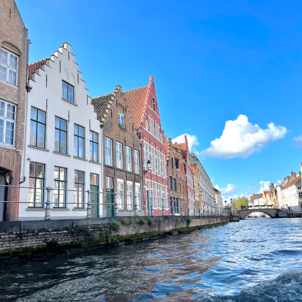View of the colorful gothic style homes from the canal in Bruges, Belgium on a sunny, blue sky day