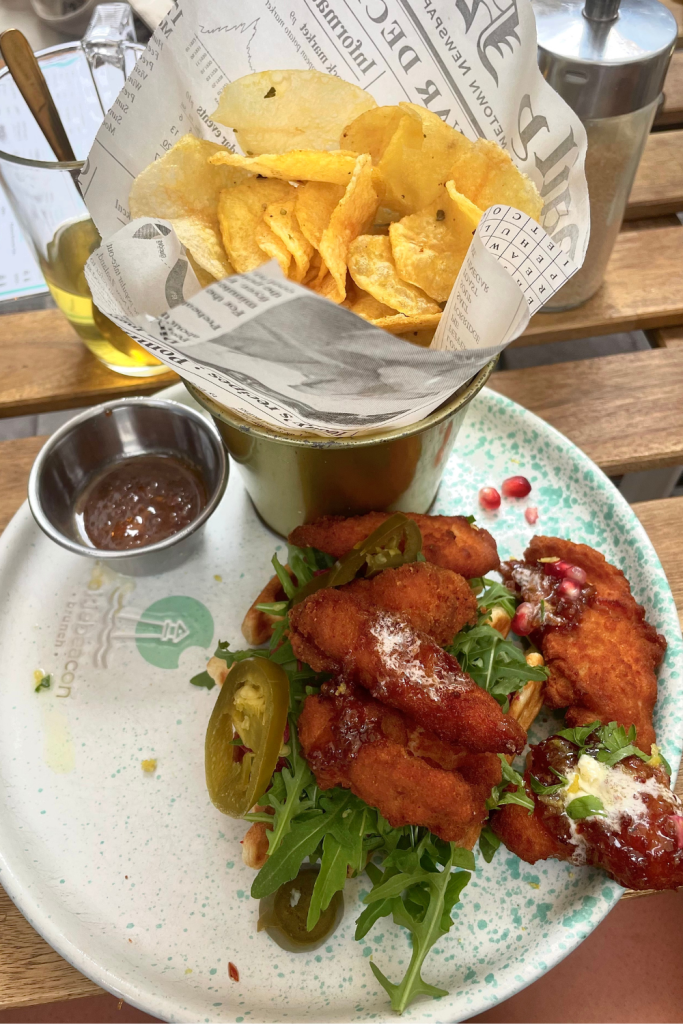 A delicious plate of fried chicken and waffles, with a side of homemade potato chips at a brunch restaurant in Budapest, Hungary.