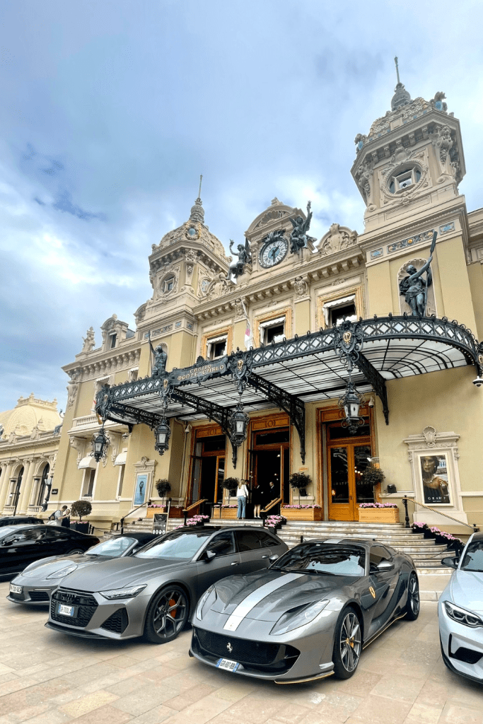 The entrance to the Monte-Carlo Casino in Monaco with many expensive cars posed in front, like a Ferari and BMW.