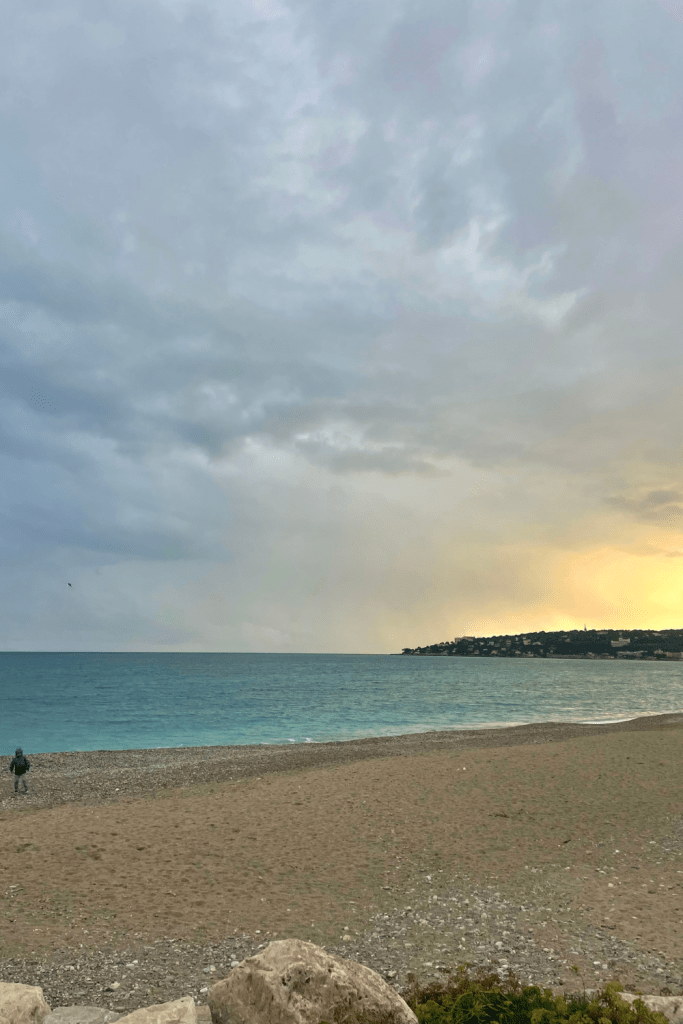 A mellow yellow sunset over the beach at Plage du Casino in Menton, France, with very light and crisp blue waters