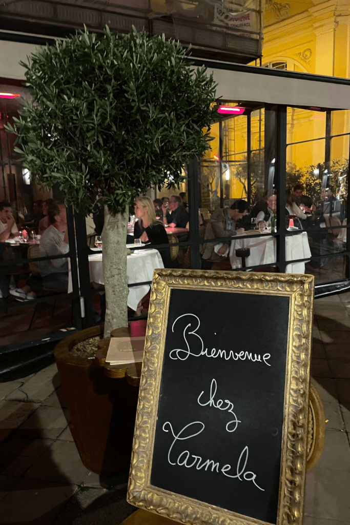 A beautiful gold and black sign in front of a restaurant in Nice, France saying "Bienvenue chez Carmela", or "Welcome to Carmela's" in English.