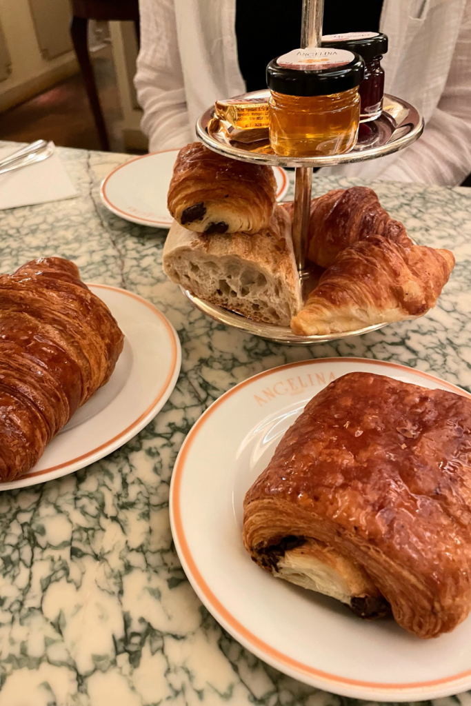 A display of mini croissants and mini pain au chocolats with a side of a baguette, honey, and jam at Angelina's Café in Paris