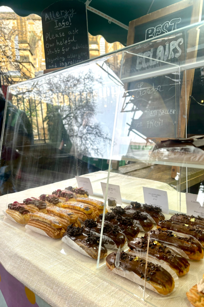 A display case of the best éclairs in London at Borough Market, featuring four different flavors of extravagantly decorated éclairs.