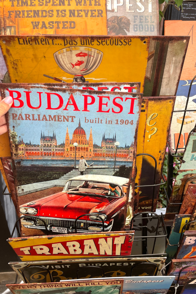 A vintage poster found at an artisant market showing a vintage car in front of the Parliament during sunset in Budapest, saying "Budapest Parliament, built in 1904".