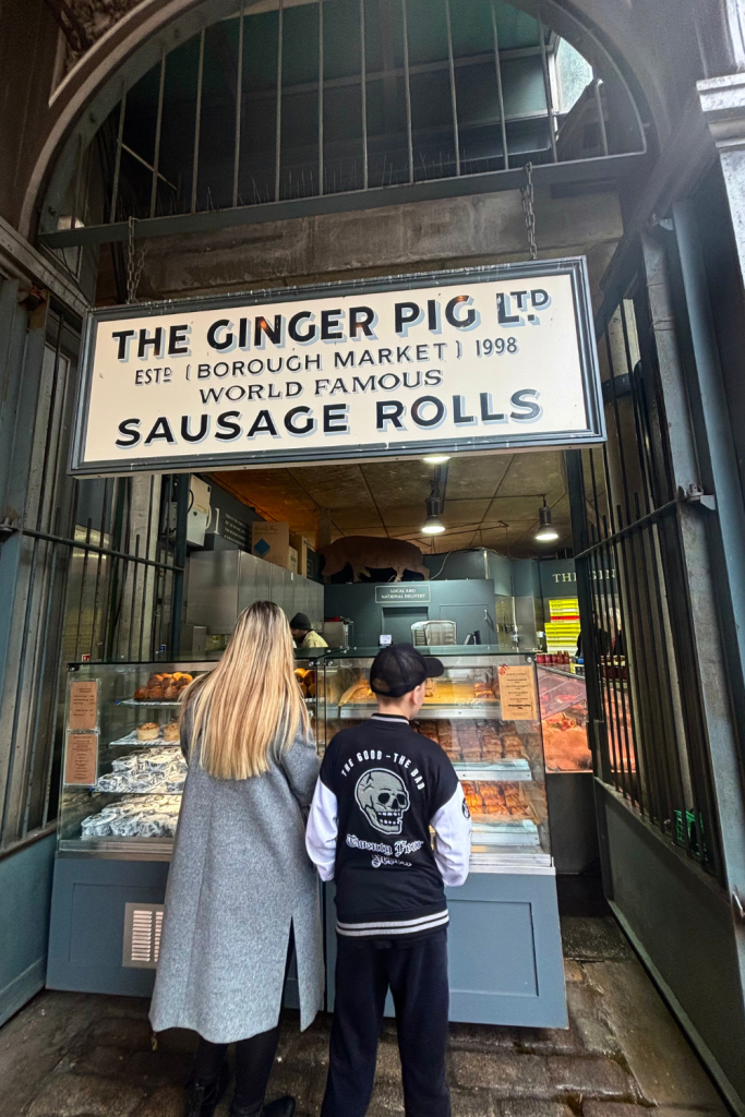 A mom and son standing in front of the sausage roll stand, deciding on what to order at the Borough Market in London, England