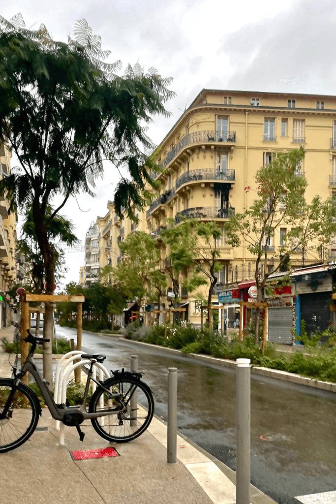 The cozy streets of Nice, France on a rainy day, lined with green trees and a bicycle.