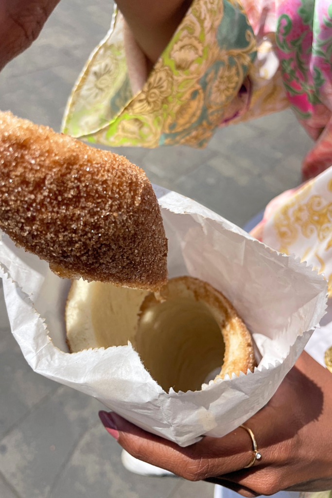 A woman pulling apart a chimney cake topped with cinnamon sugar in the streets of Budapest, Hungary.