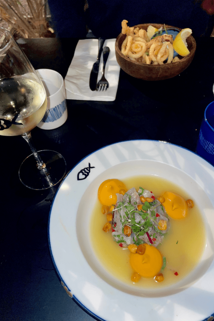 The tastiest ceviche, made with white fish and garnished with a sweet potato purée, and corn nuts. A glass of white wine in the background. At a restaurant in Nice, France