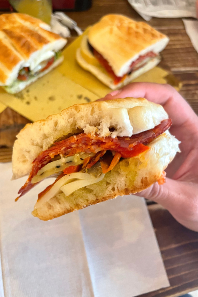 A hand holding a classic Italian ciabatta sandwich filled with roasted vegetables and Italian meats from a restaurant in Rome, Italy