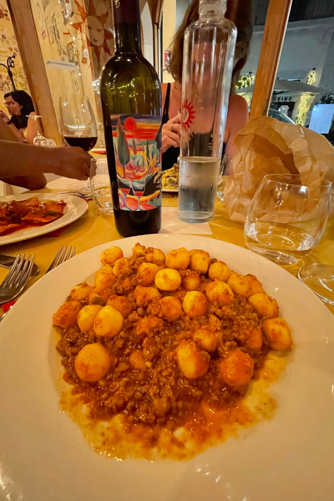 Gnocchi bolognese at a Tuscan restaurant in Rome, Italy with a bottle of red wine in the background