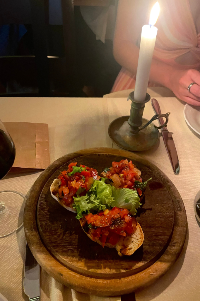 Three pieces of bruschetta on a wooden serving board with a candle in the background at a beautiful restaurant in Florence, Italy