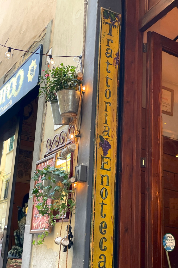 The entrance of a restaurant in Florence, Italy, with a cute wooden sign that says Trattoria Enoteca