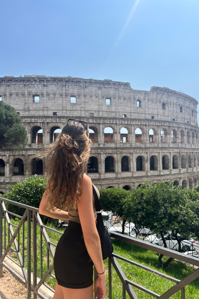 A woman in her young 20's looking off into the distance at the Roman Colosseum on a sunny day in Rome, Italy.