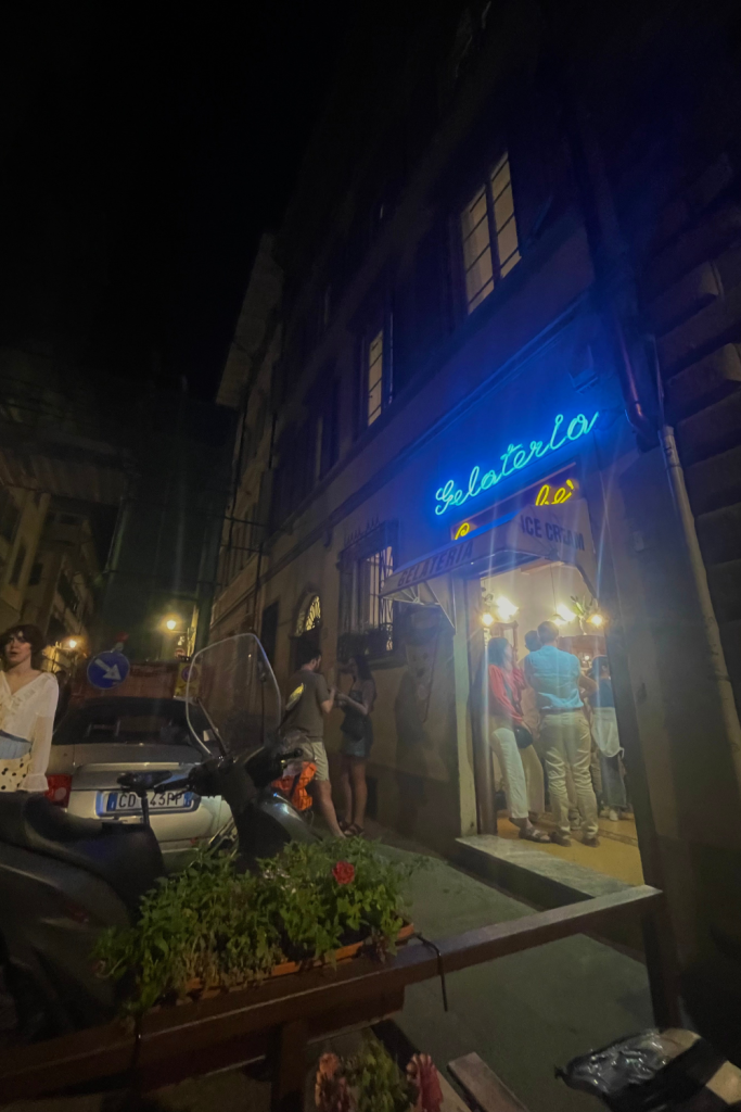 The store front of an authentic gelateria in Florence Italy at night with a neon blue sign saying gelateria