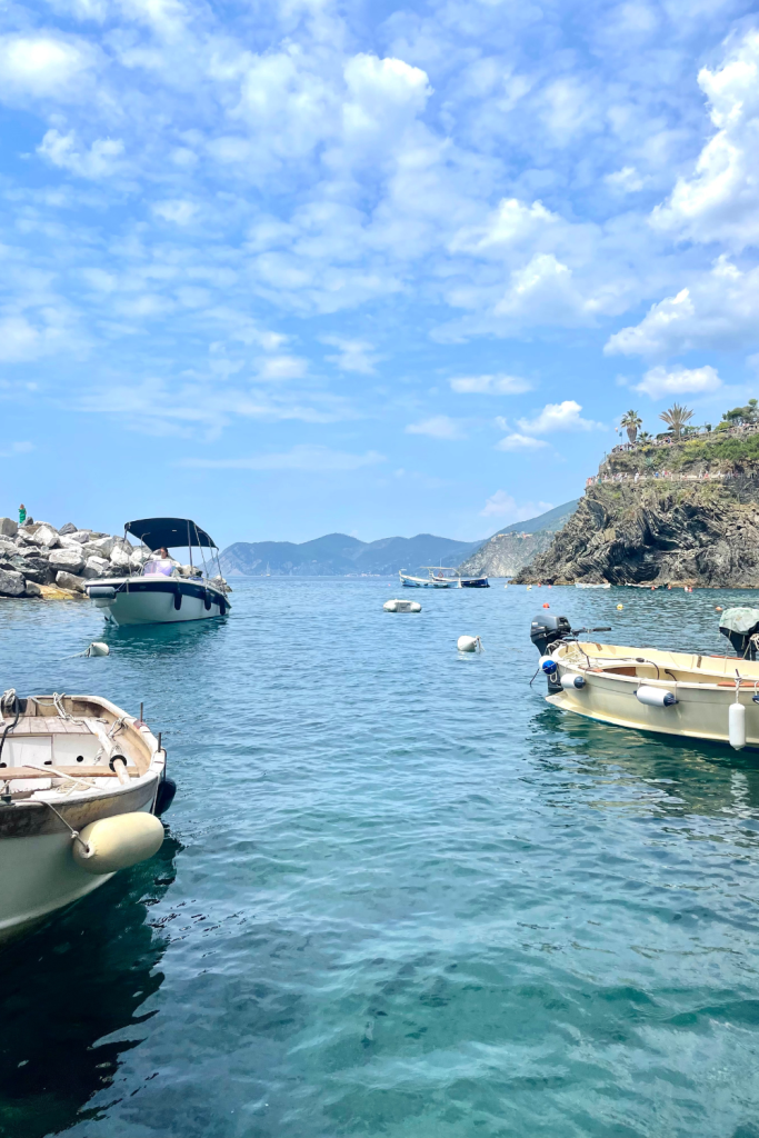 A view of the Mediterranean Sea with a few boats scattered in the foreground, off the coast of Cinque Terre in Italy on a sunny, blue sky day.