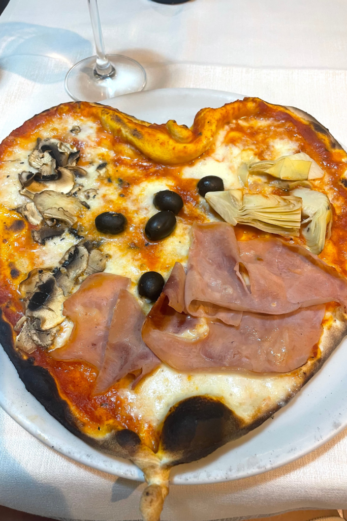 A homemade pizza in the shape of a heart, cooked in a wood fire oven, topped with mushrooms, olives, ham, and artichokes, from a restaurant in Florence, Italy