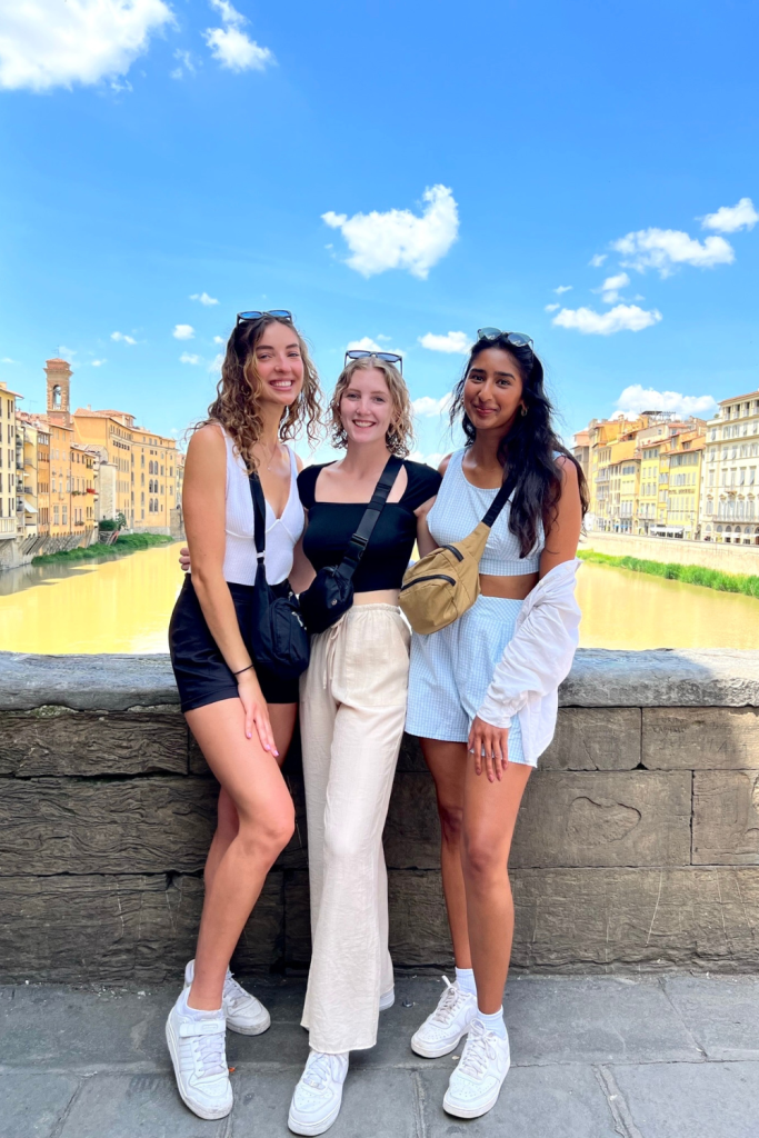Three best friends smiling for a photo in front of Ponte Vecchio on a sunny day in Florence, Italy